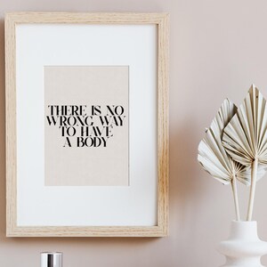 Puede incluir: Una impresi&oacute;n enmarcada con el texto "THERE IS NO WRONG WAY TO HAVE A BODY" sobre un fondo beige. El marco es de madera clara y la impresi&oacute;n est&aacute; colgada en una pared rosa claro.