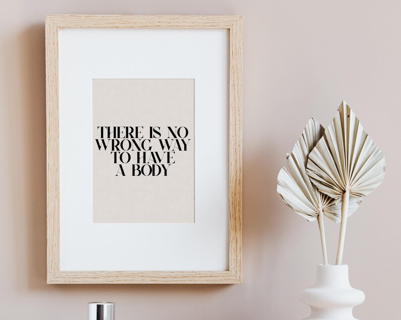 Puede incluir: Una impresi&oacute;n enmarcada con el texto "THERE IS NO WRONG WAY TO HAVE A BODY" sobre un fondo beige. El marco es de madera clara y la impresi&oacute;n est&aacute; colgada en una pared rosa claro.