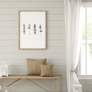 May include: A framed watercolor print of four stylized trees in shades of green against a white background. The print is hanging on a white shiplap wall. Two brown patterned throw pillows are on a wooden bench in front of the print.