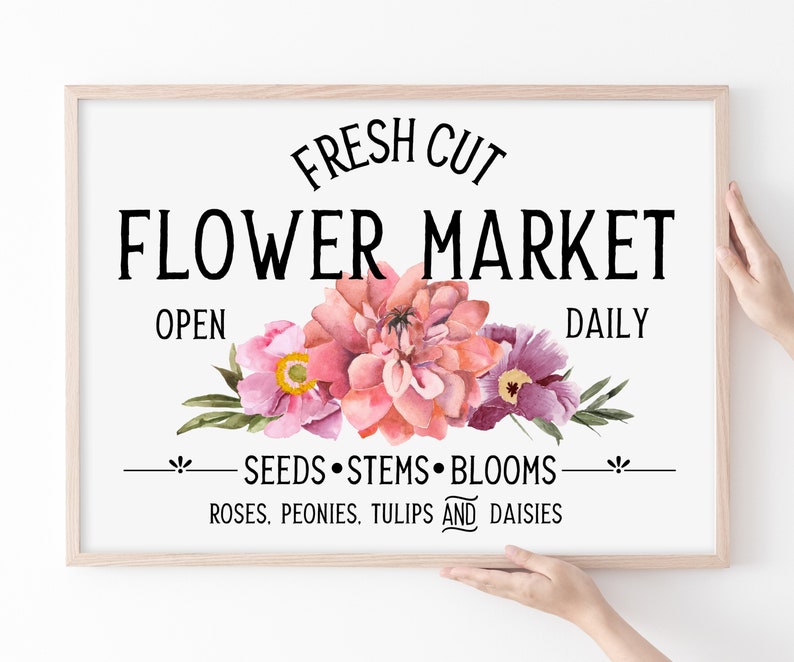 May include: A framed sign with the text "FRESH CUT FLOWER MARKET OPEN DAILY" and a floral design featuring pink, purple, and green flowers. The text below the flowers reads "SEEDS STEMS BLOOMS ROSES, PEONIES, TULIPS AND DAISIES."