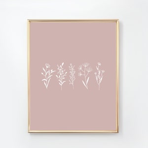May include: A digital print with a minimalist design featuring white line drawings of various flowers and plants on a blush pink background. The print is framed in a gold frame.