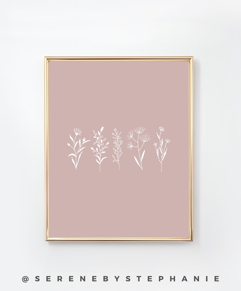 May include: A digital print with a minimalist design featuring white line drawings of various flowers and plants on a blush pink background. The print is framed in a gold frame.