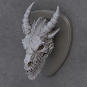 May include: A detailed, white dragon skull sculpture with prominent horns and sharp teeth, mounted on a grey plaque. The sculpture has a textured surface and is set against a neutral background, showcasing the intricate details of the fantasy-themed decor.