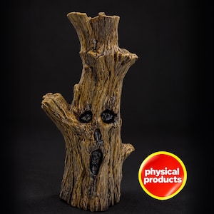 May include: A brown tree stump sculpture with a textured bark surface and a carved face featuring hollowed-out eyes, a nose, and an open mouth. A circular red sticker with a yellow border displays the white text physical products.