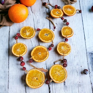 Puede incluir: Una guirnalda hecha de rodajas de naranja secas y bayas rojas sobre un fondo de madera blanca.