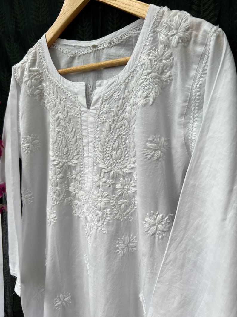 Puede incluir: T&uacute;nica blanca de algod&oacute;n con intrincados bordados blancos con motivos florales y paisley. La t&uacute;nica tiene un escote en V y mangas tres cuartos.