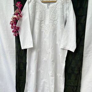 Puede incluir: T&uacute;nica blanca de algod&oacute;n con intrincados bordados blancos. El bordado presenta un dise&ntilde;o floral con un motivo central y peque&ntilde;os detalles florales en todo el dise&ntilde;o.