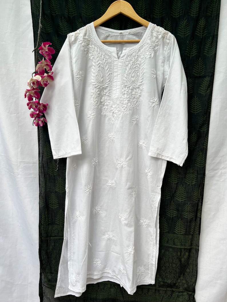 Puede incluir: T&uacute;nica blanca de algod&oacute;n con intrincados bordados blancos. El bordado presenta un dise&ntilde;o floral con un motivo central y peque&ntilde;os detalles florales en todo el dise&ntilde;o.