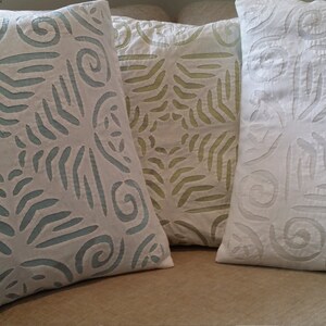以下が含まれることがあります： 白地に青、緑、白のエンボス加工が施された装飾的なクッションが3つあります。