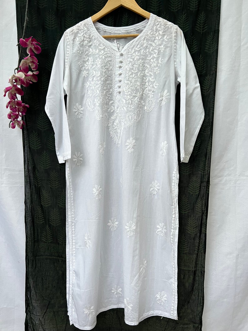 Puede incluir: T&uacute;nica blanca de algod&oacute;n con intrincados bordados blancos con dise&ntilde;os florales. La t&uacute;nica tiene un escote redondo y mangas largas.