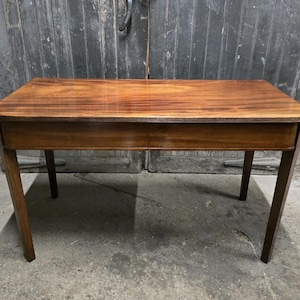 May include: A rectangular wooden table with a rich, reddish-brown finish. The table has a smooth surface, a single drawer, and four slender legs. The table measures approximately 122 cm long and 61 cm wide.