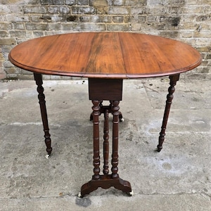 May include: An antique wooden drop-leaf table with a circular top and dark brown finish. The table features turned legs and small caster wheels. The table's top is approximately 122 cm in diameter when fully extended.