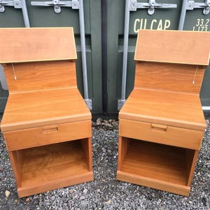 May include: Two wooden bedside tables in a warm, reddish-brown hue. Each table has a drawer and an open shelf. The top section has a slanted design. The tables are made of wood and have a simple, modern design. Dimensions are approximately 60 cm high.