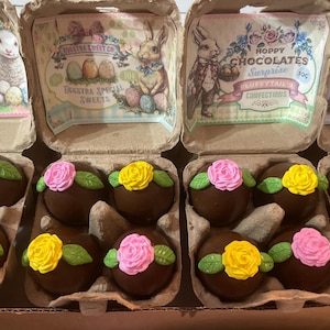 May include: Chocolate Easter egg treats decorated with pink and yellow roses and green leaves, presented in cardboard egg cartons. The cartons feature vintage-style illustrations of bunnies, lambs, and chicks, with text that reads "Eggstra Special Sweets" and "Hoppy Chocolates Surprise."