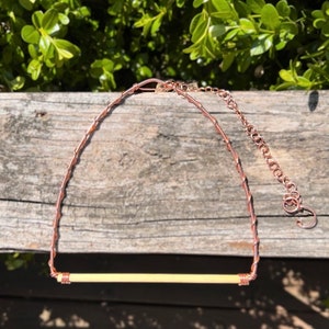 May include: A necklace featuring a horizontal, cylindrical, cream-coloured bead secured by copper wire wrapping. The necklace includes a copper wire chain and a metal extender chain with a circular clasp, showcasing a metallic copper finish throughout.