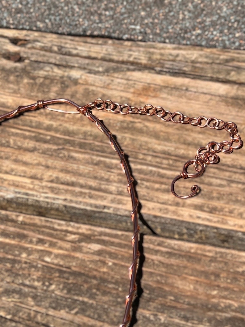 May include: A copper-coloured wire necklace featuring a twisted wire design and an adjustable chain extension with a hook clasp. The necklace is constructed from a single strand of wire wrapped in a spiral pattern, ending in a series of circular links.