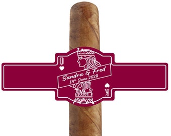 May include: A brown cigar with a burgundy label featuring a Queen of Hearts design and the text "Sandra & Fred 14th June 2028". The cigar is set against a white background.