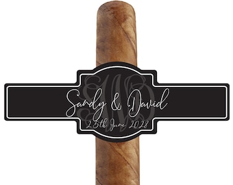 May include: A brown cigar with a decorative black label. The label features the names "Sandy & David" and the date "25th June 2022" in white script. The cigar is set against a white background.