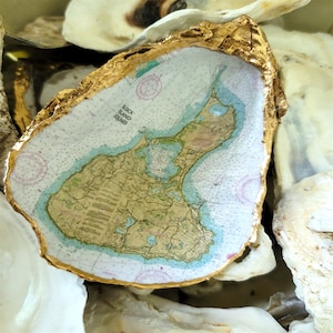 May include: A gold-leafed oyster shell with a map of Block Island Sound inside. The map is printed on a white background with blue and green accents.