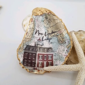 May include: A gold-trimmed oyster shell with a nautical map design featuring a lighthouse and the text "New London Ledge".