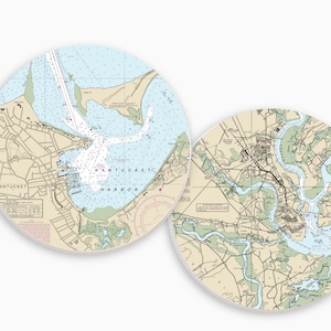 May include: Two round coasters featuring nautical charts. One coaster displays Nantucket Harbor, with the town's name visible. The other coaster shows a detailed map of a coastal area. Both have a light blue and beige color scheme.