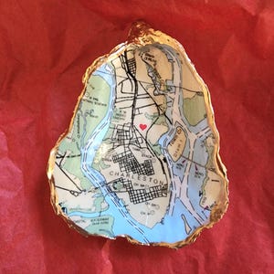 May include: A gold-leafed oyster shell with a map of Charleston, South Carolina inside. A red heart is marked on the map.