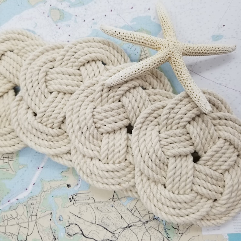 K&ouml;nnte beinhalten: Ein Set aus drei geflochtenen Korkuntersetzern in nat&uuml;rlicher Cremefarbe. Die Untersetzer sind in Wellenform angeordnet und aus dickem, geflochtenem Seil gefertigt.