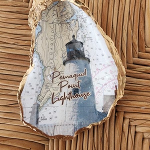 Puede incluir: Una concha de ostra con pan de oro con un mapa náutico y una imagen de un faro. El texto "Pemaquid Point Lighthouse" está impreso en la concha.