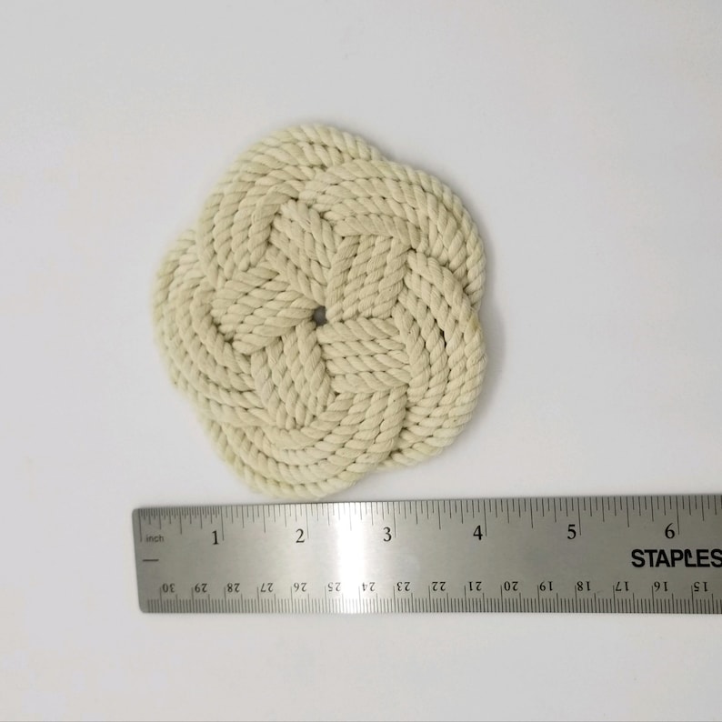 K&ouml;nnte beinhalten: Nahaufnahme eines runden, geflochtenen Untersetzers aus beigefarbenem Seil. Der Untersetzer hat einen Durchmesser von etwa 7,5 cm.