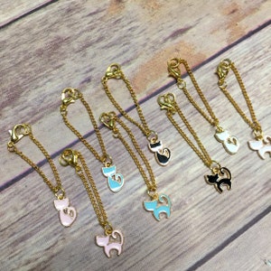 May include: Eight gold chains with cat charms. The charms are in various colors, including pink, blue, black, and white. Each charm features a stylized cat silhouette.