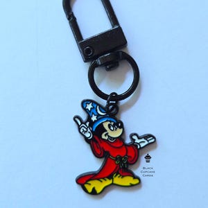 May include: A black metal keyring featuring a cartoon Mickey Mouse charm in a wizard outfit. The charm is coloured red, yellow, blue, and white. The keyring has a lobster clasp and a small ring.