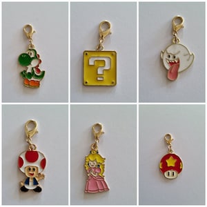 Può includere: Sei diversi tiretti per cerniere dorati che rappresentano personaggi del franchise di videogiochi Super Mario Bros. I tiretti per cerniere includono Yoshi, un blocco con un punto interrogativo, Boo, Toad, la principessa Peach e un fungo rosso.