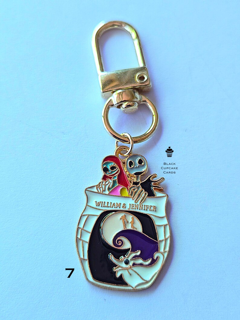 May include: A gold-colored keychain with a decorative charm featuring characters from "The Nightmare Before Christmas." The charm has a white border and includes the text "WILLIAM & JENNIFER." The design incorporates a moon, a bat, and other elements.