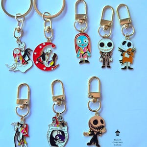 May include: Collection of gold-toned keychains featuring characters from "The Nightmare Before Christmas." Designs include Jack Skellington, Sally, and other characters. Each keychain has a lobster clasp for easy attachment. The keychains are colorful and detailed.