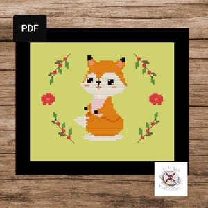 Op de afbeelding: Een kruissteekpatroon met een schattige oranje vos met een witte buik en een bloemenkrans eromheen. Het patroon is op een lichtgroene achtergrond.