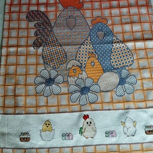 K&ouml;nnte beinhalten: Ein K&uuml;chentuch mit einem bunten gestickten Design mit zwei H&uuml;hnern und K&uuml;ken. Die H&uuml;hner sind blau und grau mit orangefarbenen K&auml;mmen und die K&uuml;ken sind gelb. Der Hintergrund ist ein kariertes Muster aus Orange und Wei&szlig;.