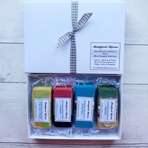 May include: A white gift box with a gray and white checkered ribbon. The box contains four bars of handmade soap. The soap bars are labeled with the names "Perfect Man", "Creedence", "Sherlock", and "Ginger, Amber & Bergamot".