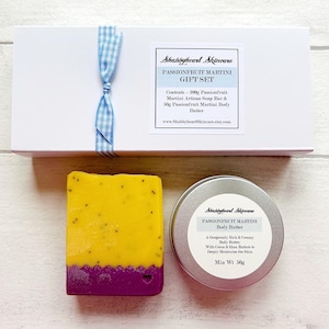 May include: A gift set containing a yellow and purple soap bar and a silver tin of body butter. The set is presented in a white box with a blue and white ribbon. The label on the tin reads "Passionfruit Martini Body Butter" and the label on the box reads "Passionfruit Martini Gift Set".