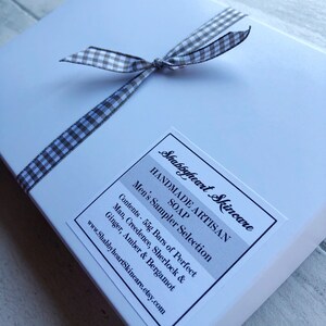 May include: A white box with a brown and white gingham ribbon tied around it. The box has a label that says "Shabbyheart Skincare Handmade Artisan Soap Men's Sampler Selection Contents - 55g Bars of Perfect Man, Creedence, Sherlock & Ginger, Amber & Bergamot www.ShabbyheartSkincare.etsy.com"