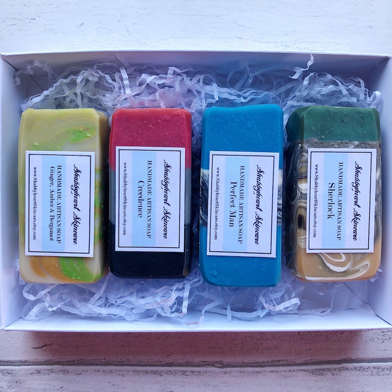 May include: Four bars of handmade artisan soap in a white box with shredded paper. The soaps are labeled with the names "Sherlock", "Perfect Man", "Creedence", and "Ginger, Amber & Bergamot".