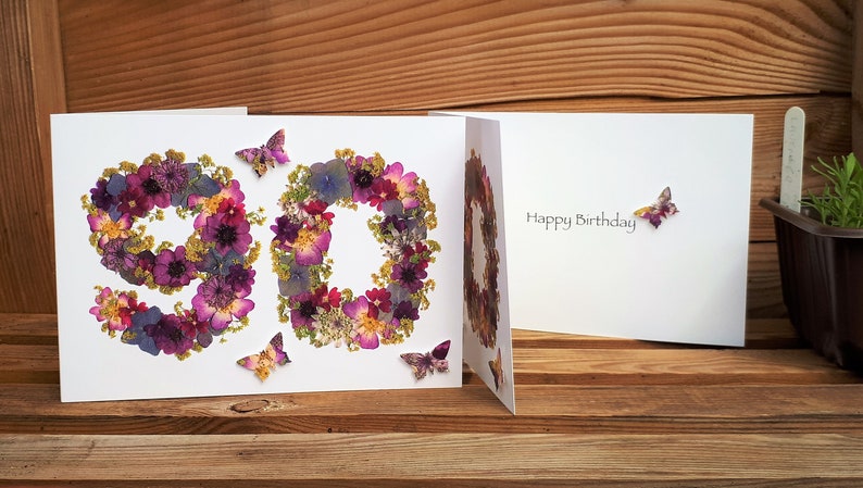 May include: A white card with the number 90 made of pressed flowers and butterflies. The inside of the card says "Happy Birthday".