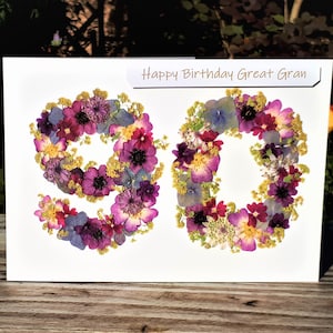 May include: A white card with the words "Happy Birthday Great Gran" printed on it. The number 90 is made from pressed flowers in shades of purple, pink, blue, and yellow.
