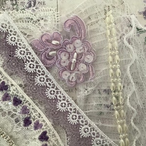 Può includere: Un assortimento di pizzi e abbellimenti delicati nei toni del bianco e della lavanda. Include finiture di perline, applicazioni floreali ricamate con paillettes e vari bordi in pizzo con motivi a cuore e geometrici. Una fornitura artigianale di ispirazione vintage.
