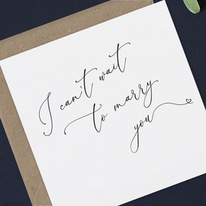 May include: A white card with black calligraphy that reads "I can't wait to marry you" with a small heart at the end of the cursive writing.