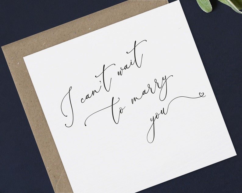 May include: A white card with black calligraphy that reads "I can't wait to marry you" with a small heart at the end of the cursive writing.