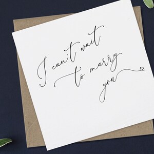 May include: A white card with black calligraphy that reads "I can't wait to marry you" with a small heart symbol at the end.