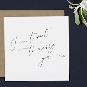 May include: A white card with black calligraphy that reads "I can't wait to marry you" with a small heart symbol at the end.