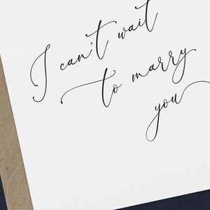 May include: A white card with black calligraphy that reads "I can't wait to marry you" with a small heart symbol at the end.