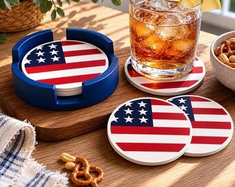 May include: A set of drink coasters featuring the American flag design. The coasters have a white base with red and white stripes and a blue field with white stars. A blue coaster holder is also included.