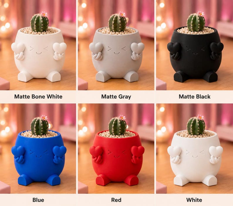 May include: A collection of small, colorful planters, each shaped like a character with a smiling face and heart-shaped hands. Each planter holds a small cactus. Colors include matte bone white, gray, black, blue, red, and white. Text on the image reads "Matte Bone White", "Matte Gray", "Matte Black", "Blue", "Red", and "White".